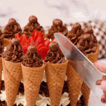 a person is cutting an ice cream cone cake with chocolate frosting and strawberries on top