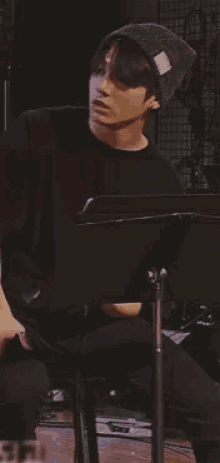 a man wearing a black shirt and a beanie is sitting in front of a microphone .