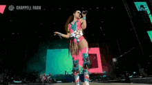 a woman in a colorful outfit is singing into a microphone on a stage with the word chappell roan in the corner