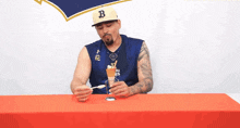 a man wearing a hat with the letter b on it holds a spoon