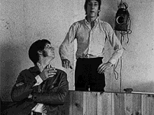two men are standing next to each other in a black and white photo . one man is holding a gas mask .