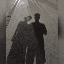shadows of two people standing next to each other on the street