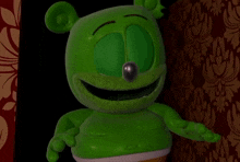 a green gummy bear with blue eyes is standing in front of a patterned wall