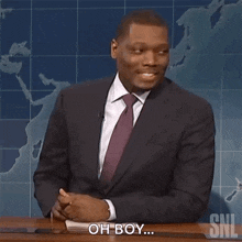a man in a suit and tie is sitting at a desk and saying oh boy