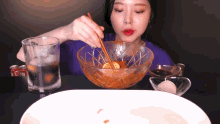 a woman is eating a bowl of food with chopsticks next to a glass of soda
