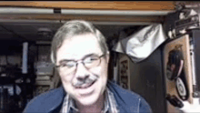 a man wearing glasses and a mustache is smiling in a room .