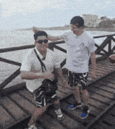 two men are standing on a wooden dock and one of them is wearing sunglasses