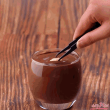 a person is dipping a piece of chocolate into a glass of chocolate sauce
