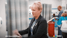 a woman in a suit is standing in a hospital room with a nbc logo on the bottom
