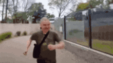 a man is walking down a sidewalk with a shoulder bag .