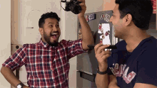 a man taking a picture with a camera while another man holds a cell phone