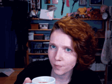 a woman with red hair is holding a cup in front of a screen that says 73