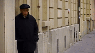 a man wearing a flat cap and a black coat is standing on a sidewalk