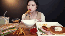 a woman is sitting at a table eating a sandwich and pancakes with a fork .