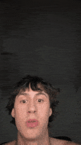 a man without a shirt is making a funny face with his mouth open .
