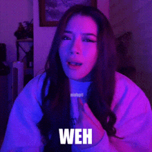 a woman is making a funny face in front of a purple and blue background with the word weh written on it .