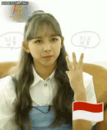 a girl with long hair is sitting on a couch and making a peace sign with her hand .