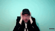 a man wearing a hat and glasses is holding his head ..