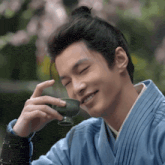 a man in a blue robe is drinking from a green cup and smiling