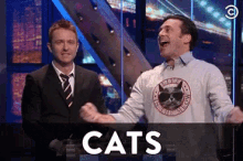 two men shaking hands in front of a screen that says cats on it