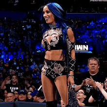 a woman with blue hair stands in front of a crowd with a sign that says wn on it