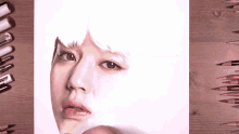 a drawing of a woman 's face is on a wooden table with colored pencils