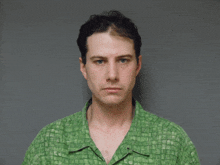 a man in a green shirt looks at the camera with a serious look on his face