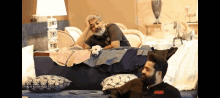two men sitting on a couch with one wearing a black shirt that says ' aar ' on it