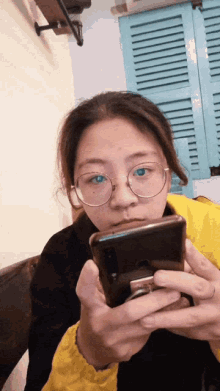 a girl with glasses is holding a cell phone