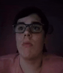 a person wearing glasses and a pink shirt is making a funny face with their mouth open .