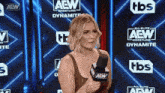 a woman holding a microphone in front of a wall that says aew