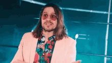 a man with long hair and sunglasses is wearing a pink suit