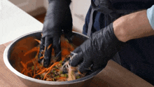 a person wearing black gloves is mixing carrots in a bowl