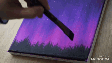 a person is painting a purple and black sky with a brush