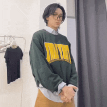 a man wearing glasses and a green sweater with a yellow lettering on it