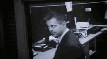 a black and white photo of a man sitting at a desk with a sticker on the wall that says " private "