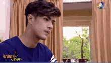 a man wearing a blue shirt that says ' a ' on it is sitting in front of a window .