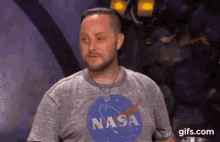 a man wearing a nasa t-shirt is sitting in front of a microphone .