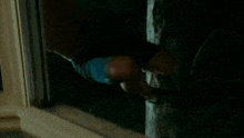 a shirtless man looks out a window with his arm outstretched