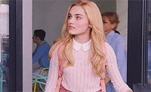 a woman wearing a pink sweater and a pink backpack is walking through a doorway .