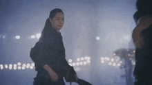 a woman in a black dress is walking down a street in the rain .