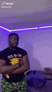 a man is standing with his arms crossed in a room with purple lights on the ceiling .