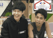 two men are smiling in front of a pinoy big brother sign