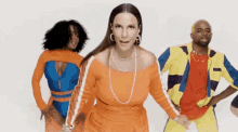 a woman in an orange dress is dancing with two men in colorful outfits .