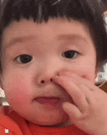 a close up of a baby 's face with his finger in his nose .