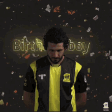 a man wearing a yellow and black shirt with the words birth boy boy behind him