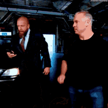 a man in a suit and tie stands next to another man in front of a car with the hashtag #thenextbigthing visible