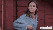 a woman in a blue jacket is standing in front of a red wall and looking at the camera .