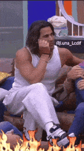 a man in a white tank top sits on a couch next to a sign that says @luna_lcdif