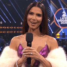 a woman holding a microphone in front of a sign that says latin grammys 2025